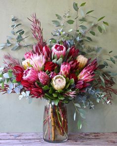 a vase filled with lots of flowers sitting on top of a wooden table next to a wall