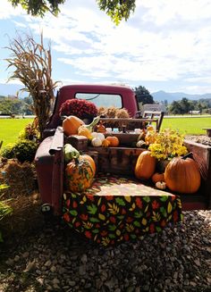 an old truck with pumpkins and gourds in the bed is parked on gravel