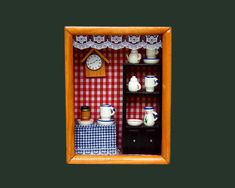 a miniature dollhouse is shown with dishes and teapots on display in an orange frame