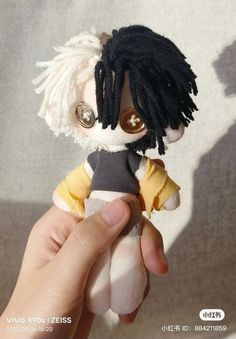 a person holding a small doll with dreadlocks on it's head and wearing a sweater