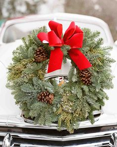 a wreath on the hood of a car with pine cones and red bow hanging from it