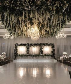 an elegant wedding setup with white flowers and greenery hanging from the ceiling, surrounded by chandeliers