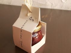 a jar of jam sitting inside of a box on top of a wooden table next to a white wall