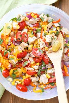 a salad with chicken, corn and tomatoes in a white bowl on top of a wooden table