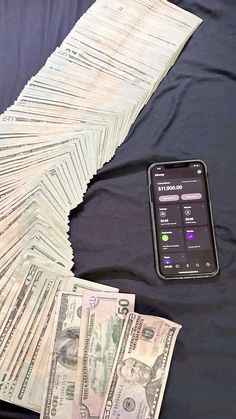 a pile of money sitting on top of a bed next to a cell phone and stack of bills