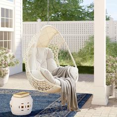 a white hanging chair on top of a blue rug in front of a porch with potted plants