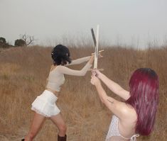 two women in short skirts are holding up swords to each other with their backs facing the same direction