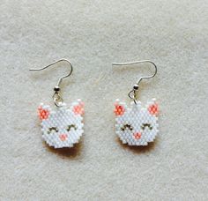 a pair of earrings with white and orange cats on them, sitting on top of a carpet