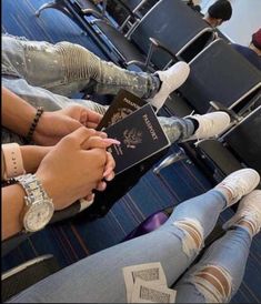 two people sitting in an airport with their feet on the ground and one holding a passport