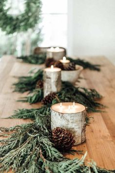 candles are lined up on a table with evergreen branches and pine cones in the middle