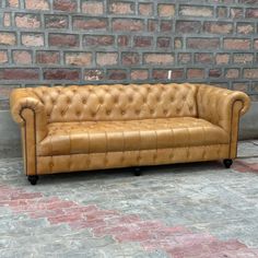 a tan leather couch sitting in front of a brick wall