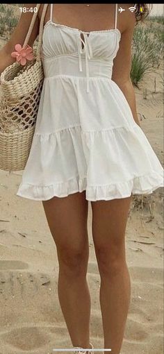 a woman standing on top of a sandy beach holding a straw bag and wearing sandals