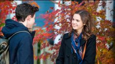 a young man and woman standing next to each other in front of trees with red leaves