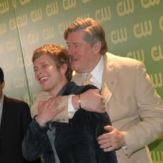 two men are hugging each other in front of a green and white wall with words on it