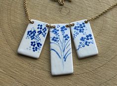 three necklaces with blue flowers on them sitting on a wooden table next to a chain