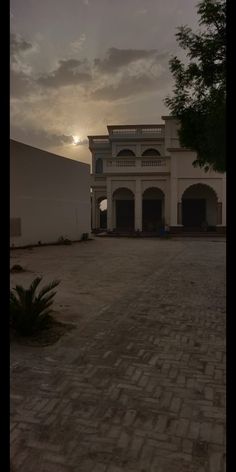 the sun is setting behind a large white building with an arched doorway and brick walkway