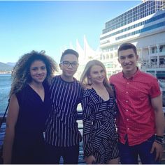 four people posing for the camera in front of a body of water