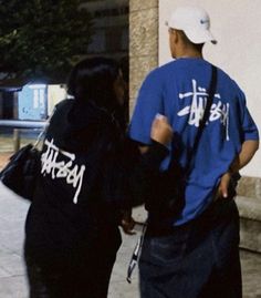 two people standing next to each other near a building with graffiti on their shirts and backpacks