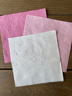 three pink and white paper napkins sitting on top of a wooden table