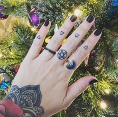 a woman's hand with tattoos and rings on it, next to a christmas tree