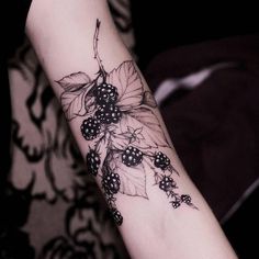 a woman's arm with blackberries and leaves tattoo on the left side of her arm