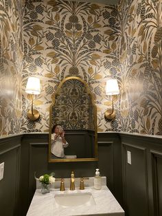 a bathroom with a sink, mirror and wallpapered walls in gold and white