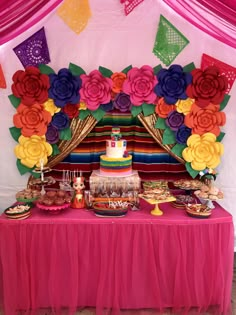 a table topped with a cake and lots of desserts next to a colorful wall