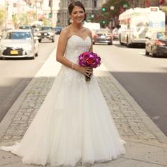 a woman in a wedding dress standing on the side of a street holding a bouquet