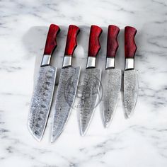 five knives are lined up on a marble counter top with red handles and silver tips