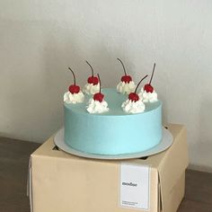 a blue cake sitting on top of a cardboard box with cherries and whipped cream