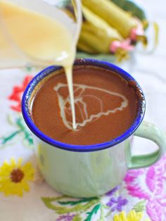 a cup of hot chocolate being poured into it with some bananas in the back ground