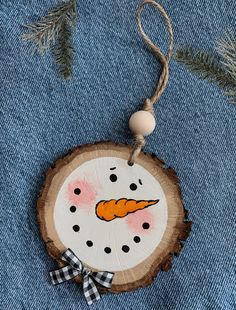 an ornament with a carrot painted on it hanging from a tree slice in the shape of a snowman