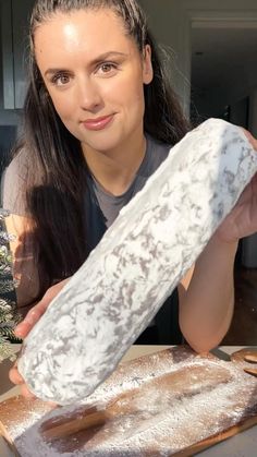 a woman holding up a large piece of bread on top of a wooden cutting board