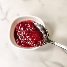 a spoon full of jam sitting on top of a white bowl next to a marble counter