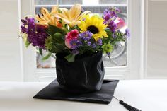 a vase filled with lots of colorful flowers on top of a white table next to a window