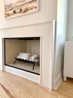 an empty fireplace in a living room with white walls and wood flooring on the side