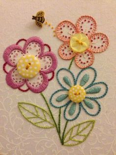 three flowers and a bee sitting on top of a white cloth covered wall hangings