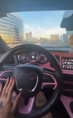 a person driving a car with pink interior and steering wheel, in front of a cityscape