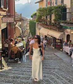 a woman in a white dress walking down a cobblestone street