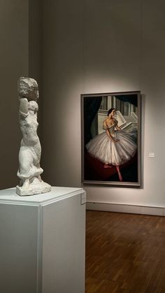 two white sculptures on pedestals in an art gallery with paintings and wood flooring