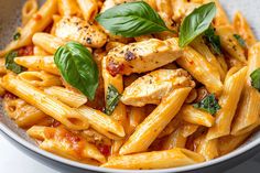 pasta with chicken, tomato sauce and basil leaves in a white bowl on a table