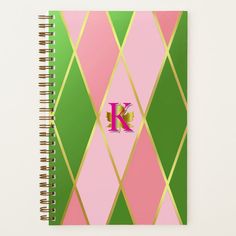 a spiral notebook with the letter k in pink, green and gold geometric design on it