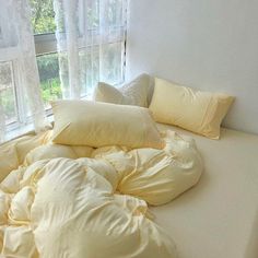 an unmade bed in front of a window with white sheets and pillows on it