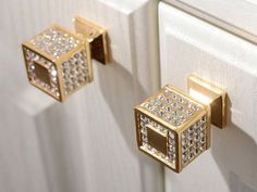 two gold and crystal knobs on a white cabinet door with diamond studded handles