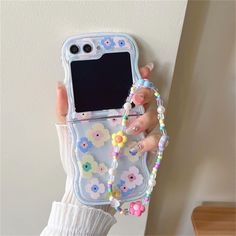 a woman holding up a cell phone case with flowers and beads attached to the back