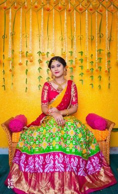 a woman sitting on top of a chair wearing a green and pink lehenga