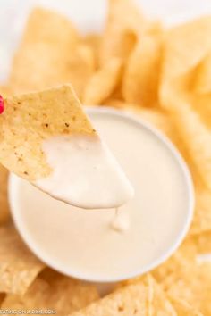 a hand holding a tortilla chip over a bowl of dip with chips in the background