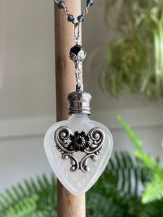 a glass heart shaped pendant hangs from a wooden pole next to a potted plant