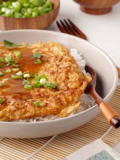 a white bowl filled with rice covered in sauce and green onions