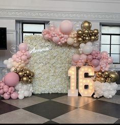 a large number surrounded by balloons and flowers in front of a wall with the number 16 on it